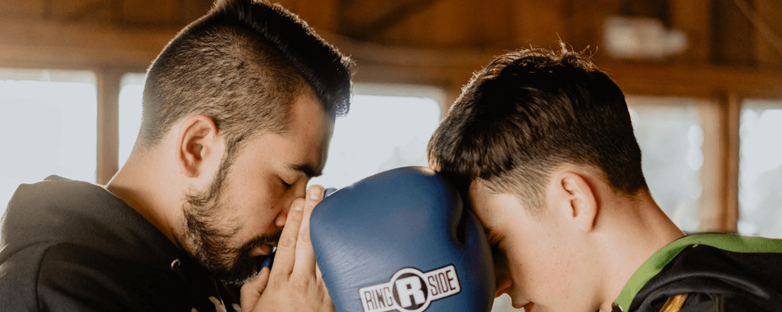 Ein Boxtrainer und sein Schüler stehen Kopf an Kopf und bereiten sich mit geschlossenen Augen auf einen Kampf vor